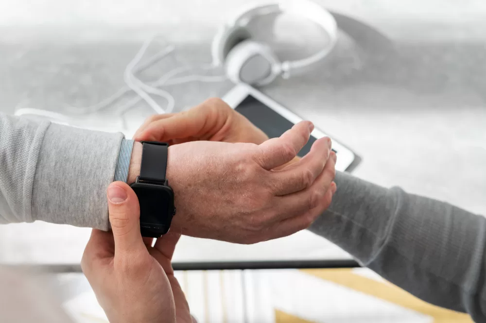 An individual assists another person with fastening a smartwatch, possibly for tracking health metrics during spinal fusion rehabilitation.