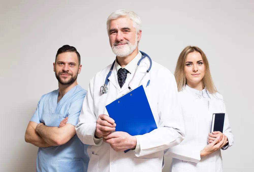 A medical team likely involved in spinal fusion rehabilitation stands together, including a doctor with a stethoscope and clipboard, a nurse in scrubs, and a specialist holding a tablet.